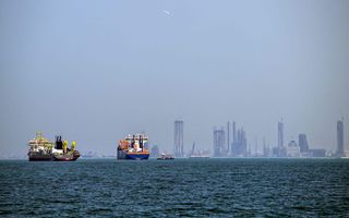 Twee grote schepen in het water met als achtergrond de skyline van een stad met wolkenkrabbers.
