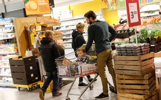 Vader doet samen met drie kinderen boodschappen. Een jong kind zit in de winkelwagen.