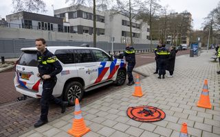 Politieagenten en een politieauto staan bij een wit-bruin schoolgebouw met grijs hekwerk eromheen.