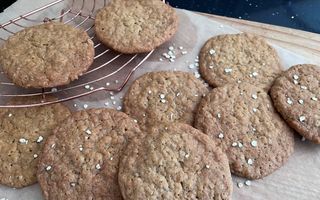 Tien robuuste koekjes op bakpapier. Een deel ligt op een koperkleurig taartrooster.