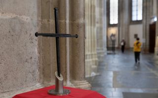 Een kruis op een zilveren voet, op een tafel met een rood kleed eroverheen.
