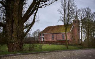Een oud kerkgebouw met een torentje, en rode dakpannen. Eromheen bomen.
