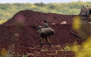 Vrouw in legeruniform draagt bepakking langs een aarden wal.