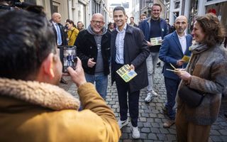 Man in blauwe jas met folders in zijn hand gaat op de foto met een man in zwarte jas.