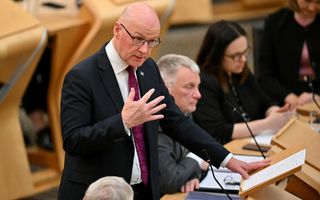 Een man in pak met een kaal hoofd spreekt achter een spreekgestoelte. 