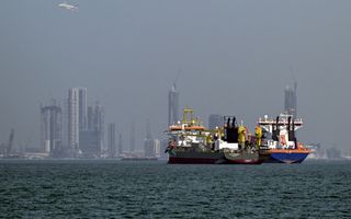 Twee schepen liggen tegen elkaar. Op de achtergrond de installaties van een haven.