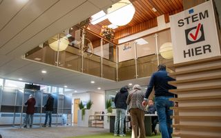 Drie mensen staan in de rij voor een tafel, waar hun stempas wordt gecontroleerd.