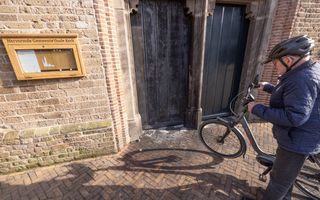 Een man met een fiets staat bij een deur met brandschade.