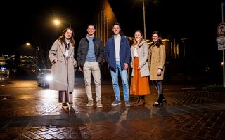 Vijf jongeren staan ’s avonds voor een kerkgebouw.