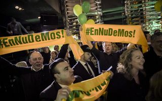 Juichende mannen en vrouwen met sjaals waarop staat: „#EnNuDeMos!”