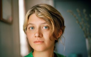 Jonge, blonde vrouw met groen vest kijkt in de camera.