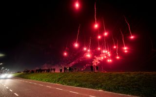Op de dijk staan honderden mensen. In de lucht grote, rode vuurballen en veel rook.