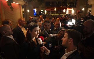 Een vrouw staat de pers te woord op een drukke bijeenkomst.