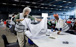 Een vrouw houdt papieren vast waarop namen en vakjes staan.