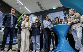 Een groep mensen kijkt met bedrukte gezichten naar een scherm met verkiezingsuitslagen.