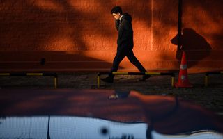 Een jongeman loopt langs een rode muur over straat in ondergaande zon. 