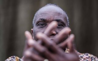 Man met donkere huid, verbergt zijn gezicht achter zijn handen. 