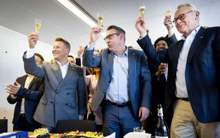 Mannen staan bij een taart en proosten met een glas wijn.