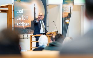 Een man in pak spreekt achter een katheder.