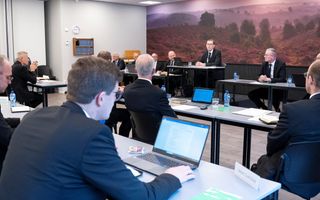 Mannen in pakken zitten achter tafels.