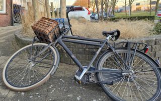 Een fiets met een krat en een RD-fietstas voorop ligt op een muurtje.