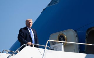 Man in donker pak met lichtblauwe stropdas staat op vliegtuigtrap.