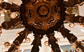Fraai bewerkte kroonluchter tegen een plafond. Je kijkt er van de onderkant tegenaan.