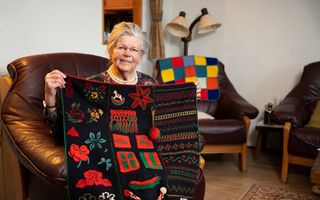 Oude dame laat haar merklap zien die ze maakte op zwarte stof en borduurde met heldere kleuren.