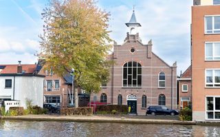 Straatbeeld van een kerkgebouw met een puntdak en een toren en een boom ervoor.