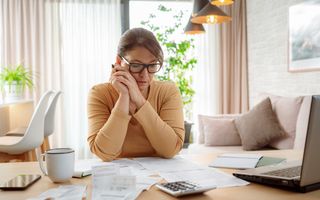 Volwassen vrouw die thuis rekeningen en belastingdocumenten bekijkt.