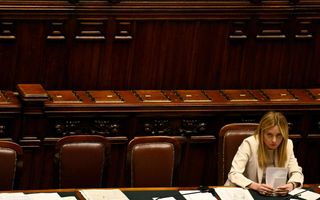 Een vrouw met een crèmekleurig jasje zit op een leren stoel achter een tafel.