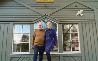 Echtpaar voor een olijfgroen, houten huis waarop een okergele plank hangt met de naam Beth Chaim.