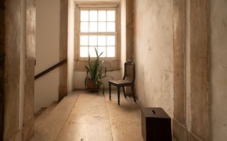 Overloop met links een trap naar beneden. De vloeren zijn van marmer. Voor het raam staan een stoel en een plant.