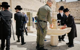 Enkele Joden, inclusief een soldaat, bevinden zich bij de Klaagmuur in Jeruzalem. Sommigen houden een beker onder de kraan.