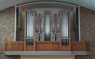 Een pijporgel hangt in een kerkgebouw. In het front zijn versieringen aangebracht.