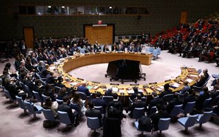 Vergaderzaal met in het midden een hoefijzervormige tafel, waar tientallen stoelen omheen staan.