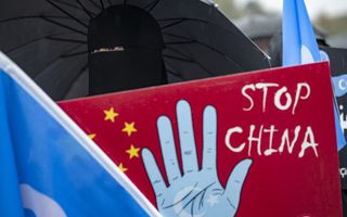 Vrouw in zwarte boerka onder een zwarte paraplu staat achter een groot rood bord met daarop een blauwe hand en de tekst: Stop China.