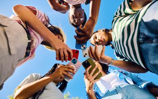 Vijf middelbare scholieren kijken buiten op hun smartphones, van onderaf gefotografeerd.