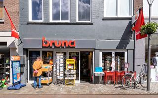 Het exterieur van een Brunawinkel waar buiten allerlei rekken staan met boeken, kaarten, kranten en artikelen in de uitverkoop.