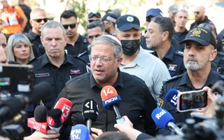 Verslaggevers houden microfoons voor een man in een zwart overhemd met wit keppeltje; hij wordt omringd wordt door andere mensen.