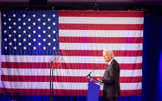 Franklin Graham, een man met grijs haar, voor een Amerikaanse vlag met rode en witte strepen en witte sterren op een blauw vlak.