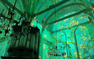 Kerkinterieur met pijporgel en kroonluchters. Op de muren is een schilderij met amandelbloesem geprojecteerd tegen een blauw-groene achtergrond.