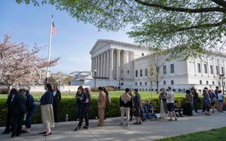 Mensen staan in een groene omgeving voor een witmarmeren gebouw dat lijkt op een Griekse tempel. 