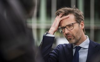 Man in pak en met bril strijkt door zijn haar