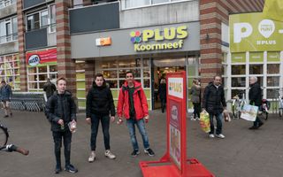 Plus-supermarkt met daarvoor mensen die boodschappen doen en drie jongeren.