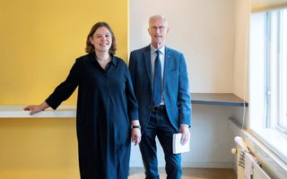 Een man en een vrouw staan lachend in een ruimte. De man heeft een boek in zijn linkerhand. 