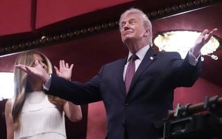 Een man in pak met blond haar staat met zijn armen wijd. 