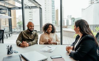 Man en vrouw met donkere huidskleur hebben een gesprek over financiën met een blanke vrouw met lang haar. 