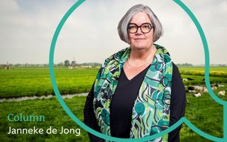 Een vrouw met kort grijs haar, een bril, zwarte kleding en een groen gedessineerde sjaal om haar schouders. Op de achtergrond een polderlandschap. 