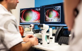 Een man in witte jas kijkt naar een monitor met een foto van een oog. 